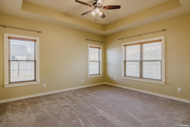 carpeted spare room with ceiling fan, a raised ceiling, and baseboards