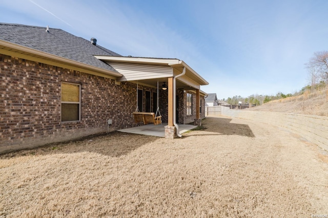 rear view of house featuring brick siding, roof with shingles, a patio area, and fence