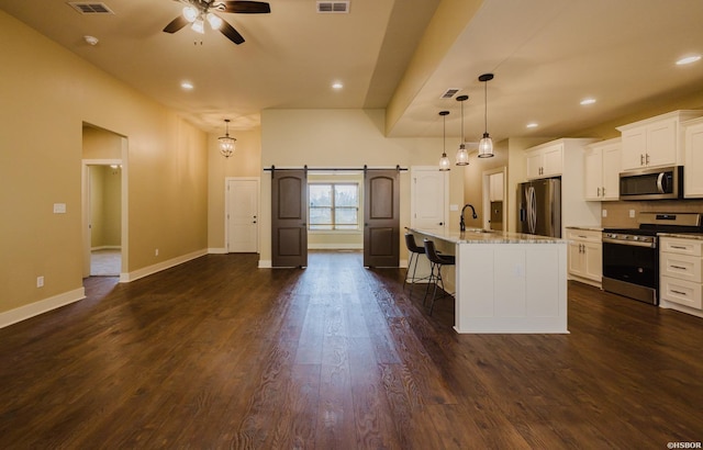 kitchen with a barn door, dark wood-style flooring, a sink, appliances with stainless steel finishes, and a kitchen bar