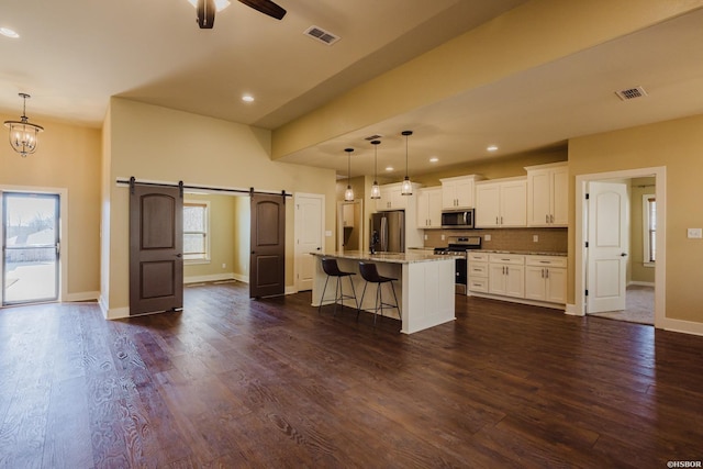 kitchen featuring a barn door, visible vents, dark wood finished floors, stainless steel appliances, and a kitchen bar