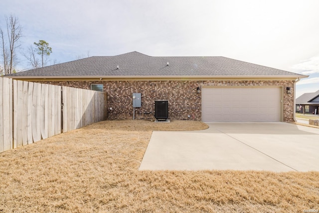 rear view of property with a garage, driveway, a shingled roof, and brick siding