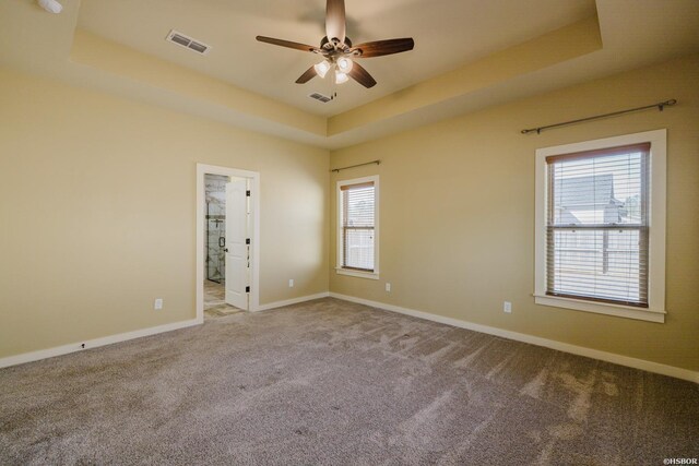 carpeted empty room with baseboards, visible vents, a raised ceiling, and a ceiling fan