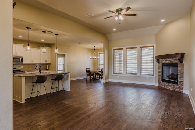 living area with dark wood-style flooring, visible vents, vaulted ceiling, a stone fireplace, and ceiling fan with notable chandelier