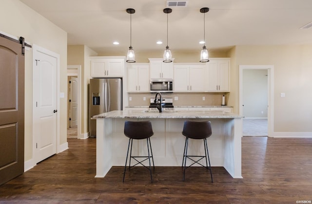 kitchen featuring dark wood-type flooring, appliances with stainless steel finishes, a barn door, and backsplash