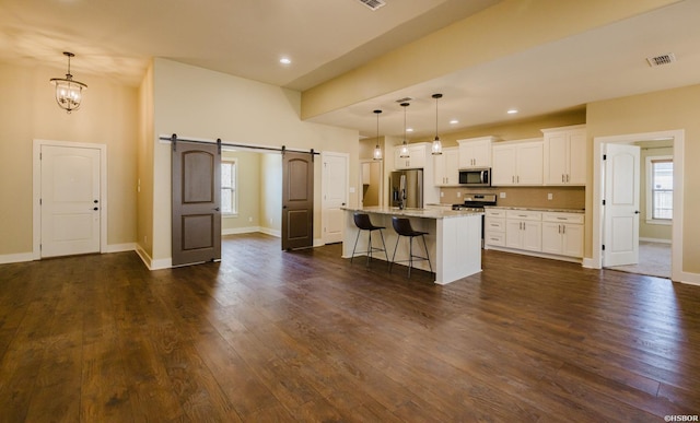 kitchen with a breakfast bar area, stainless steel appliances, visible vents, a barn door, and white cabinets