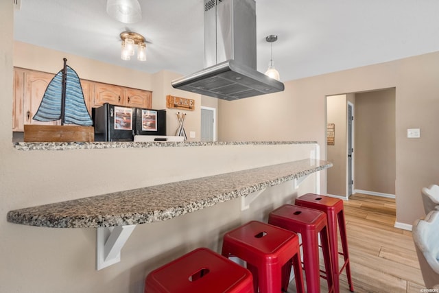 kitchen featuring island exhaust hood, baseboards, freestanding refrigerator, a breakfast bar, and light wood-style flooring