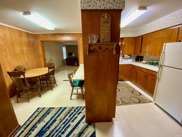 kitchen featuring brown cabinetry, freestanding refrigerator, light countertops, and wooden walls