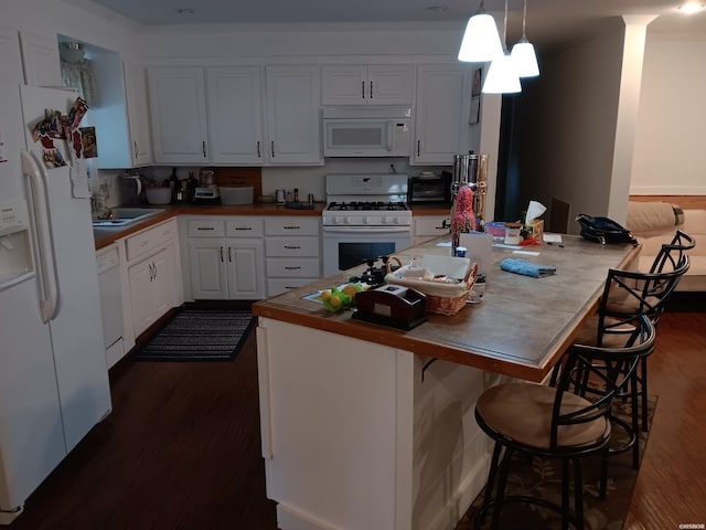 kitchen featuring white appliances, white cabinets, dark wood-style flooring, hanging light fixtures, and a kitchen bar