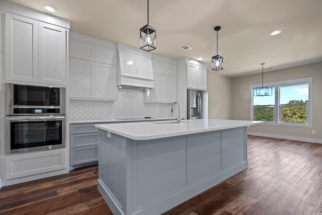 kitchen with appliances with stainless steel finishes, light countertops, hanging light fixtures, and an island with sink