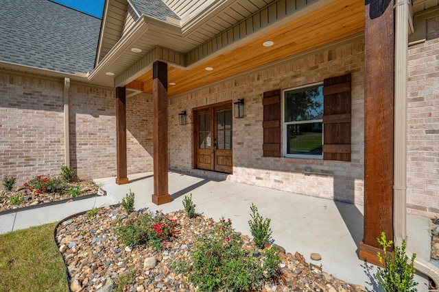 property entrance featuring covered porch, brick siding, and roof with shingles