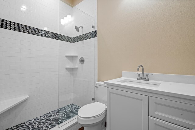 full bathroom with toilet, a tile shower, and vanity