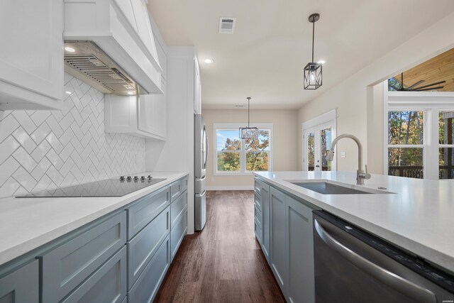 kitchen with appliances with stainless steel finishes, hanging light fixtures, custom exhaust hood, light countertops, and a sink