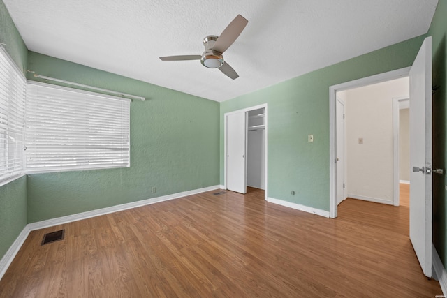 unfurnished bedroom featuring baseboards, visible vents, a textured wall, wood finished floors, and a closet