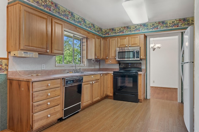 kitchen with light countertops, light wood-style flooring, an inviting chandelier, a sink, and black appliances