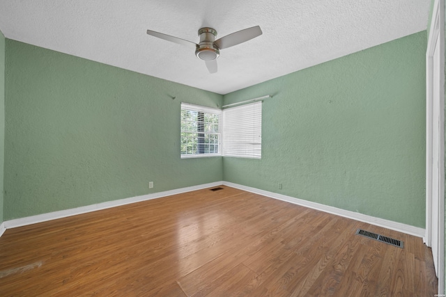 unfurnished room with visible vents, a textured wall, ceiling fan, wood finished floors, and baseboards