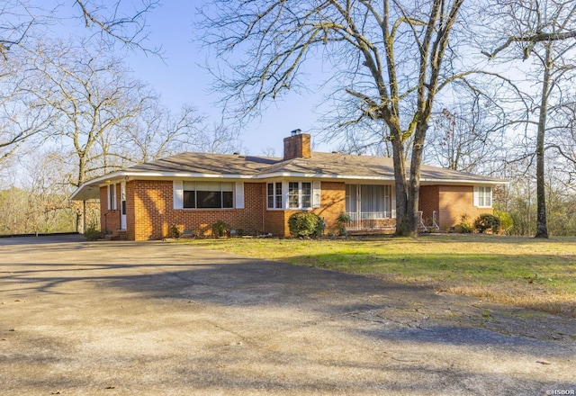 single story home with a front yard, brick siding, driveway, and a chimney