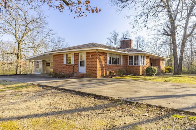 ranch-style house featuring brick siding, a chimney, entry steps, an attached carport, and driveway