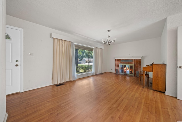 unfurnished living room featuring light wood-type flooring, an inviting chandelier, a fireplace, and visible vents