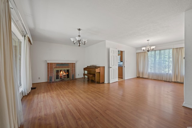 unfurnished living room featuring a brick fireplace, a textured ceiling, a notable chandelier, and wood finished floors