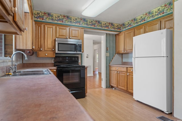 kitchen featuring light countertops, stainless steel microwave, electric range, freestanding refrigerator, and a sink