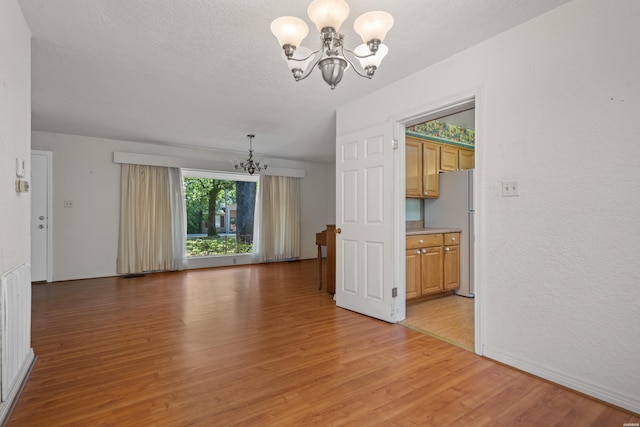 unfurnished room with a chandelier, a textured ceiling, and light wood-style flooring