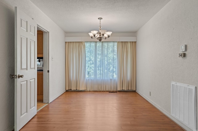 unfurnished dining area with visible vents, a textured wall, wood finished floors, a textured ceiling, and a chandelier