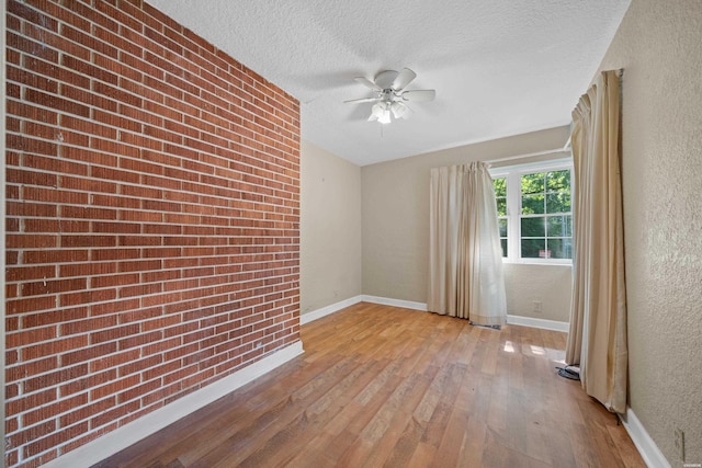 unfurnished room with brick wall, a textured wall, light wood-style flooring, and a textured ceiling