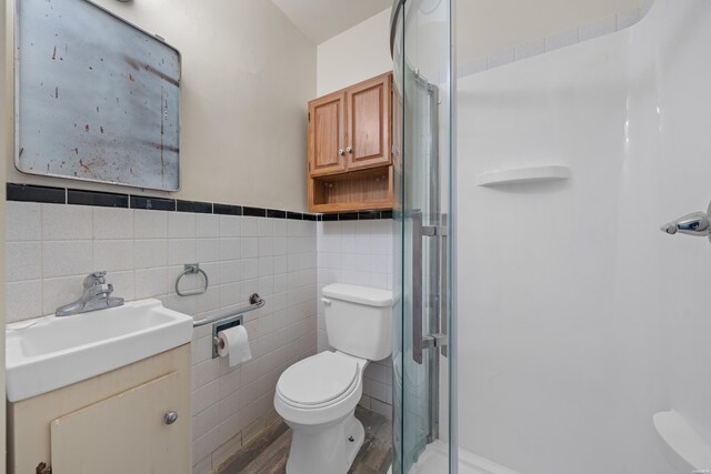 bathroom featuring tile walls, toilet, a stall shower, wainscoting, and vanity