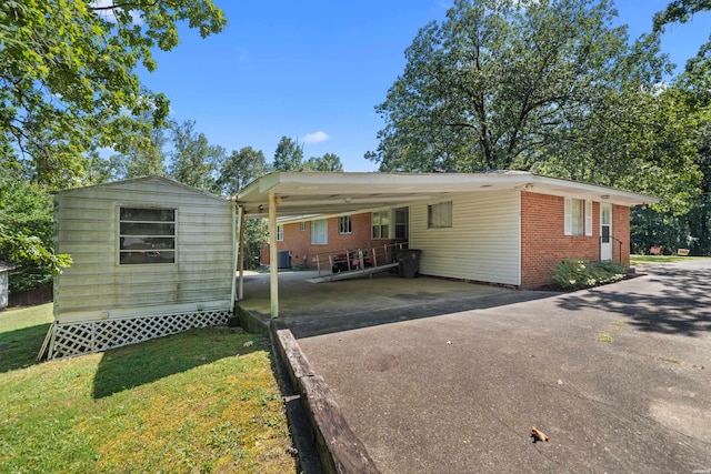 view of front of home with driveway, an attached carport, central AC, and brick siding