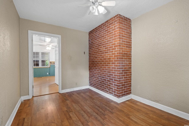 unfurnished room with a textured wall, wood finished floors, and baseboards