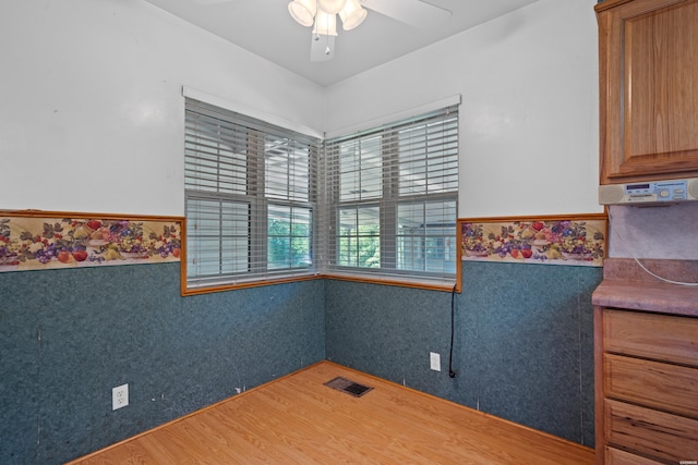 empty room with a ceiling fan, visible vents, wood finished floors, and wainscoting