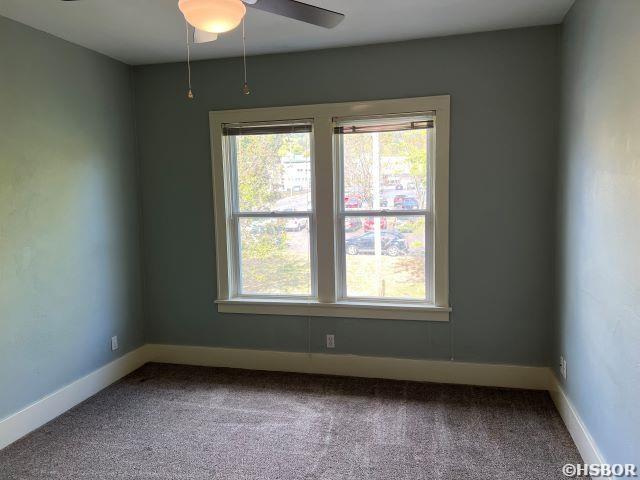 carpeted spare room featuring baseboards, a ceiling fan, and a healthy amount of sunlight