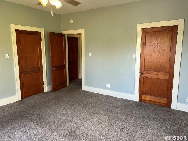 unfurnished bedroom featuring ceiling fan, dark colored carpet, and baseboards