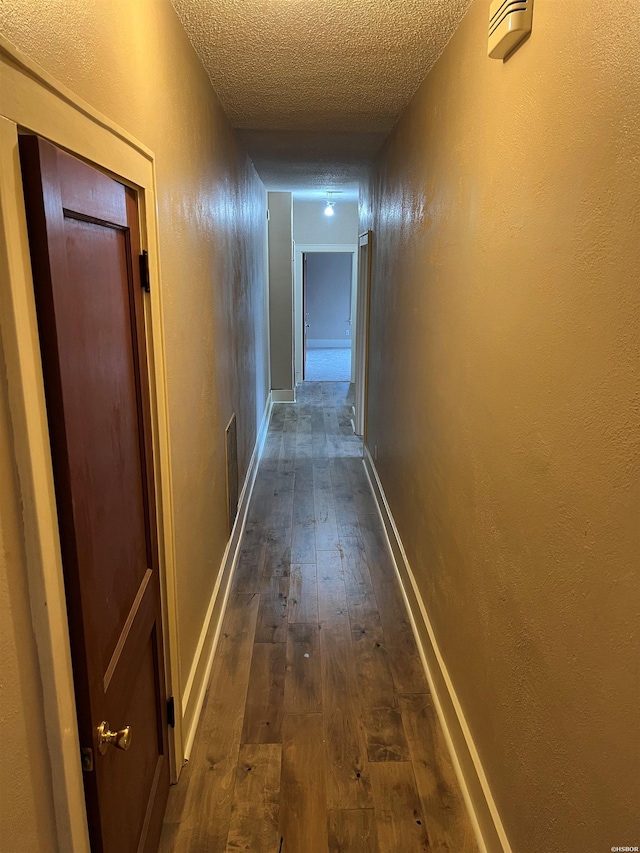 corridor featuring baseboards, dark wood finished floors, and a textured ceiling