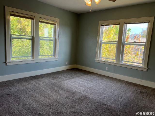 carpeted empty room featuring a ceiling fan and baseboards