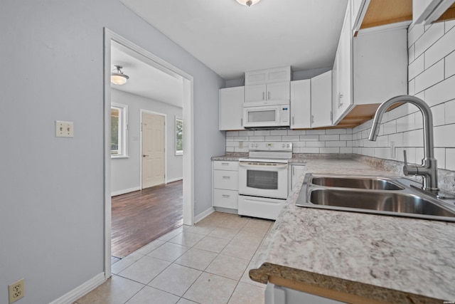 kitchen with white appliances, light tile patterned floors, a sink, white cabinetry, and backsplash