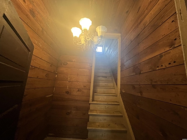 staircase featuring wood walls and an inviting chandelier