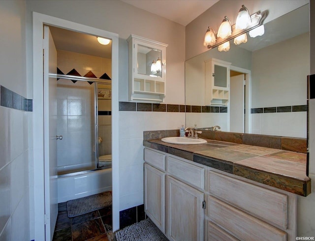 bathroom featuring tile walls, bath / shower combo with glass door, toilet, and vanity