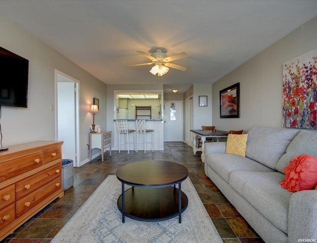 living room featuring baseboards, a ceiling fan, and stone tile flooring
