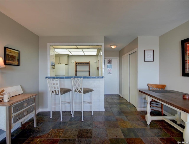 kitchen featuring stone tile flooring, a kitchen breakfast bar, and baseboards