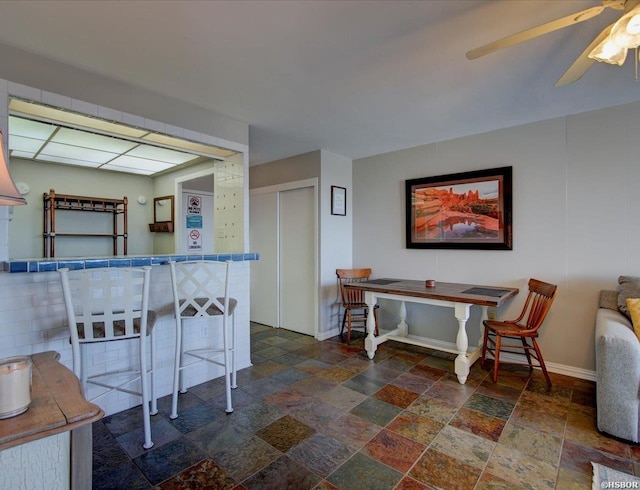 kitchen with a ceiling fan, baseboards, and stone tile floors