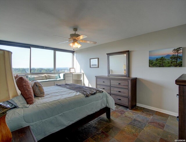bedroom featuring stone tile floors, baseboards, and ceiling fan