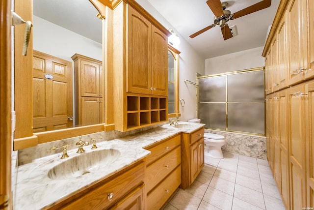 full bathroom featuring double vanity, bath / shower combo with glass door, a sink, tile patterned flooring, and toilet