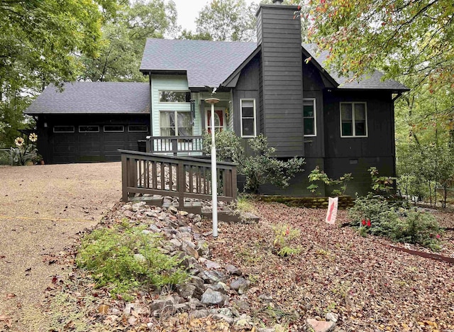 rear view of house featuring a garage, a chimney, concrete driveway, and roof with shingles