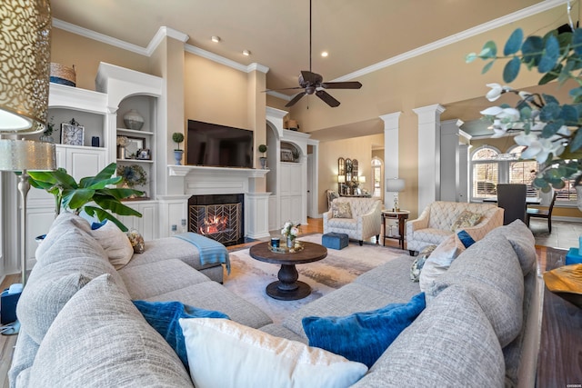 living area featuring a fireplace with flush hearth, built in shelves, crown molding, and ornate columns