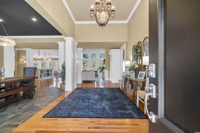 foyer featuring a chandelier, wood finished floors, a towering ceiling, decorative columns, and crown molding