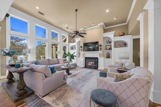 living room featuring built in features, visible vents, ornamental molding, wood finished floors, and a lit fireplace