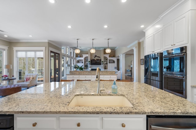 kitchen featuring appliances with stainless steel finishes, open floor plan, a sink, and decorative columns