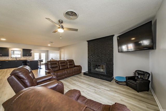 living room featuring a ceiling fan, visible vents, light wood finished floors, a fireplace, and a textured ceiling