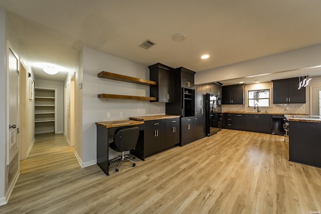 kitchen featuring dark cabinetry, light wood-style flooring, visible vents, and a sink